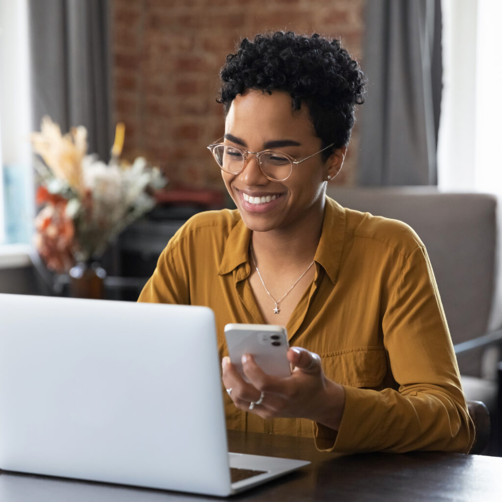 Smiling woman holding a phone and looking at a laptop